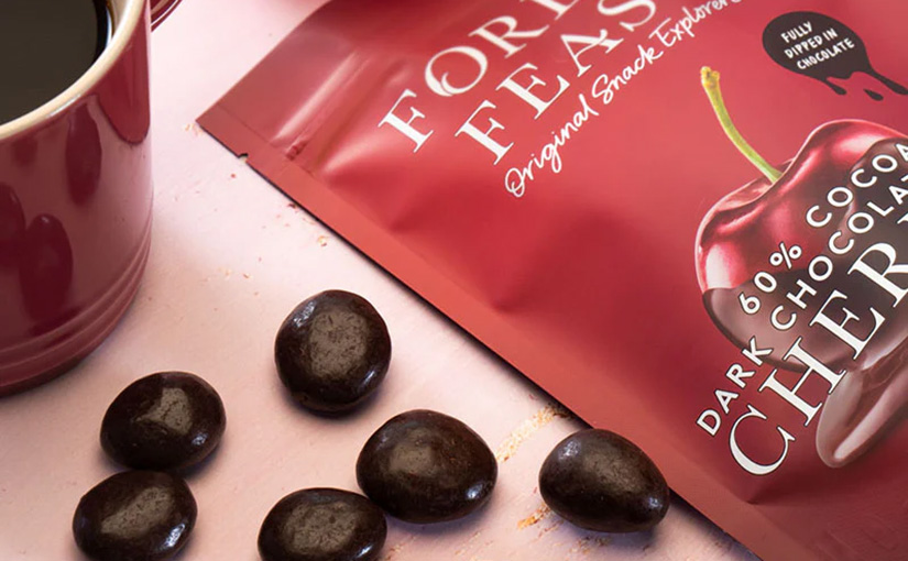 A partial view of a bag of Forest Feast dark chocolate cherries next to some spilled cherries